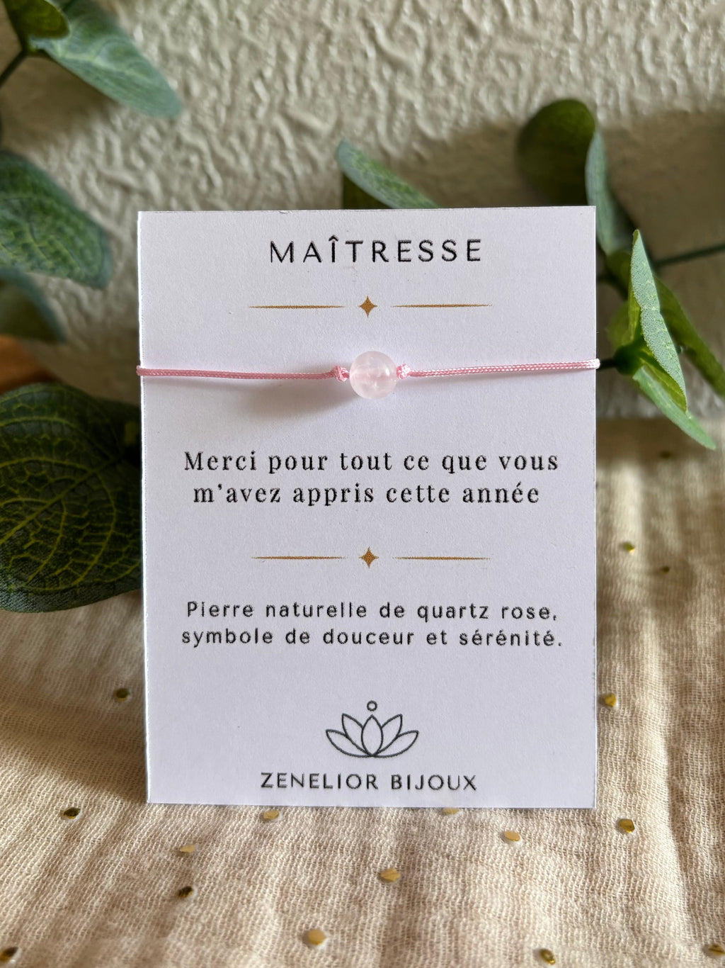 Photo du bracelet maitresse version une perle de quartz rose montée sur un cordon nylon de couleur rose pale. Le bracelet est mis en valeur sur une carte de remerciement créée spécialement pour les maîtresses.